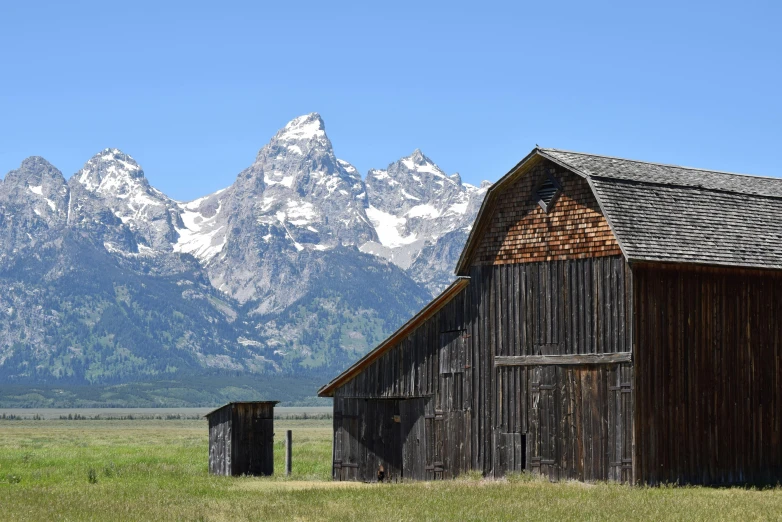 a barn in a field with mountains in the background, by Alison Geissler, unsplash contest winner, visual art, background image, wyoming, wooden houses, conde nast traveler photo