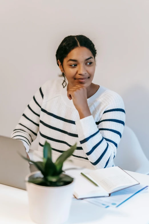 a woman sitting at a table with a laptop, wearing a white sweater, wearing stripe shirt, riyahd cassiem, curated collections