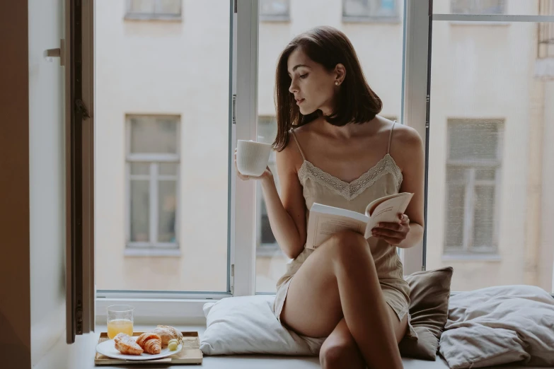 a woman sitting on a window sill reading a book, a photo, by Emma Andijewska, trending on pexels, renaissance, bralette, sitting on a mocha-colored table, having a snack, attractive face and body