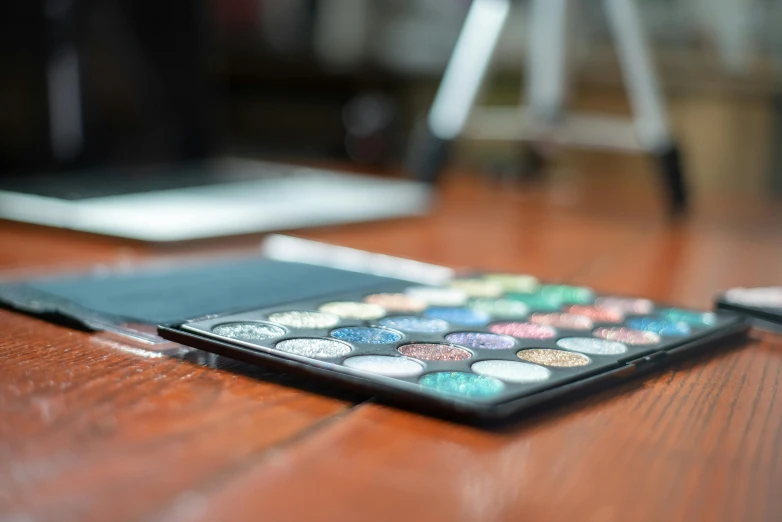 a laptop computer sitting on top of a wooden table, a photorealistic painting, by Julia Pishtar, trending on pexels, glitter makeup, palette, multicolored, black eyeshadow