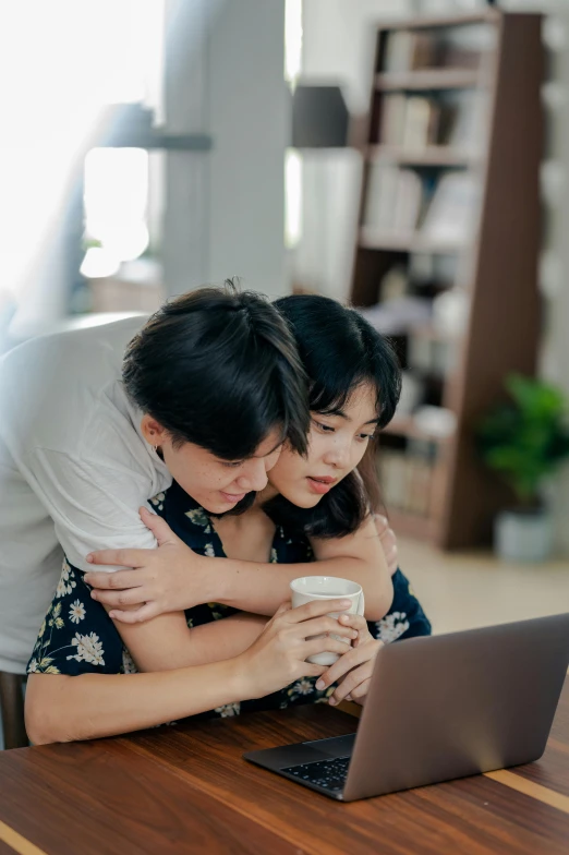 a couple of people sitting at a table with a laptop, trending on pexels, happening, hugging her knees, asian, maternal, jakarta