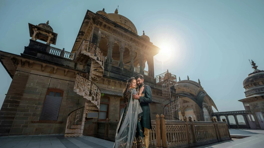 a couple standing next to each other in front of a building, by Ke Jiusi, pexels contest winner, renaissance, dressed in a jodhpuri suit, thumbnail, skies behind, sitting on a grand staircase