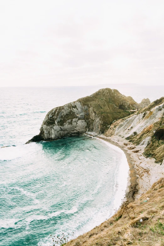 a man standing on top of a cliff next to the ocean, by Rachel Reckitt, unsplash contest winner, renaissance, chalk cliffs above, “ aerial view of a mountain, new zeeland, slightly tanned