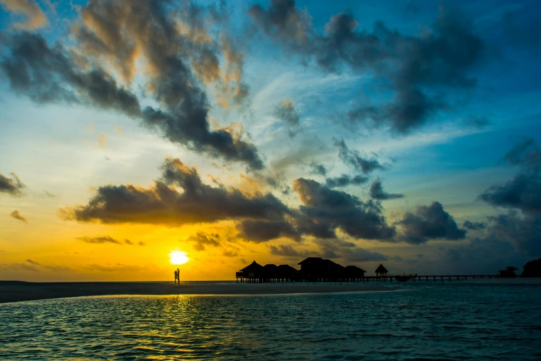 the sun is setting over a body of water, by Peter Churcher, pexels contest winner, hurufiyya, maldives in background, sunset and big clouds behind her, conde nast traveler photo, fan favorite