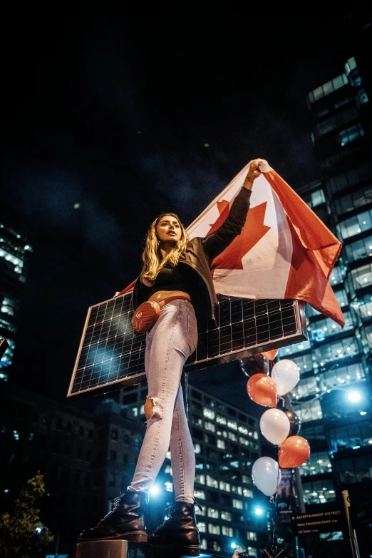 a woman standing on top of a pole holding a canadian flag, an album cover, by Julia Pishtar, pexels contest winner, happening, solar sails, subject action : holding sign, nighttime, charging through city