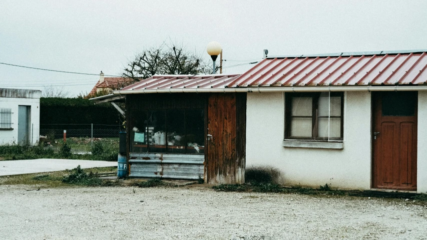 a small white building with a red tin roof, an album cover, unsplash, food stall, abandoned gas station, traveling in france, american canteen