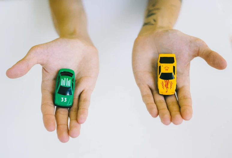 a person holding two small toy cars in their hands, unsplash, green and yellow, muscle cars, hands with five fingers, 🎨🖌️