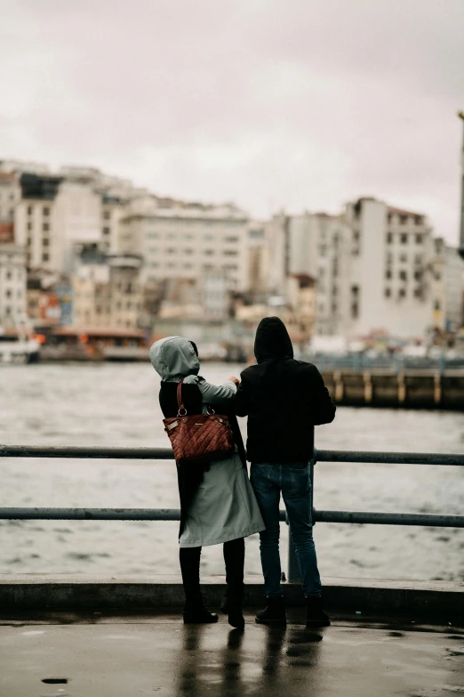 two people standing next to each other near a body of water, by irakli nadar, istanbul, a cozy, gen z, waving