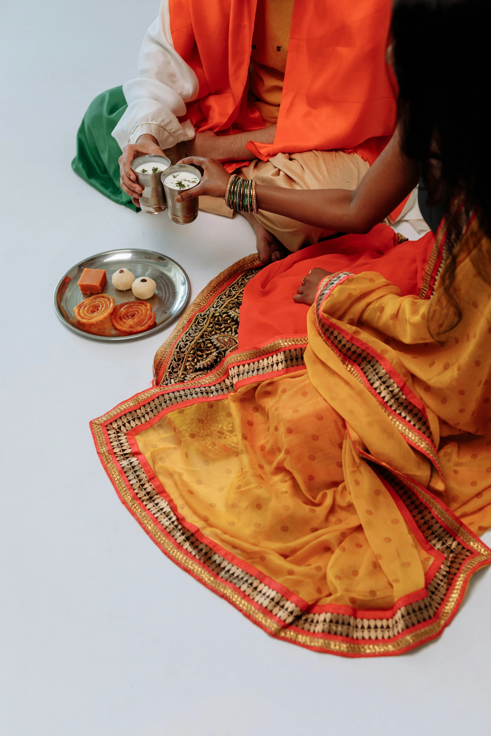 a man and a woman sitting next to each other, visual art, wearing a sari, flatlay, orange palette, close-up on legs