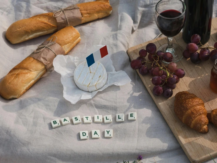 a table topped with bread and grapes next to a bottle of wine, unsplash, letterism, french flag, good day, scattered props, made of cheese
