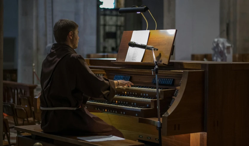 a man playing a pipe organ in a church, an album cover, by Bryan Organ, unsplash, figuration libre, wearing brown robes, sitting at desk at keyboard, live performance, 2 1 st century monk