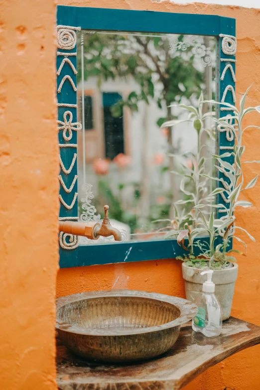 a bathroom sink sitting under a mirror next to a plant, inspired by Riad Beyrouti, pexels contest winner, outdoors setting, orange color, french village exterior, water fountain