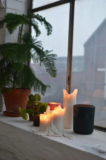 a couple of candles sitting on top of a window sill, by Jessie Algie, light and space, apartment of an art student, curated collection, at dusk at golden hour, made of glowing wax and ceramic