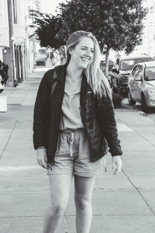 a woman riding a skateboard down a sidewalk, a black and white photo, an aviator jacket and jorts, headshot profile picture, genevieve o'reilly, happily smiling at the camera
