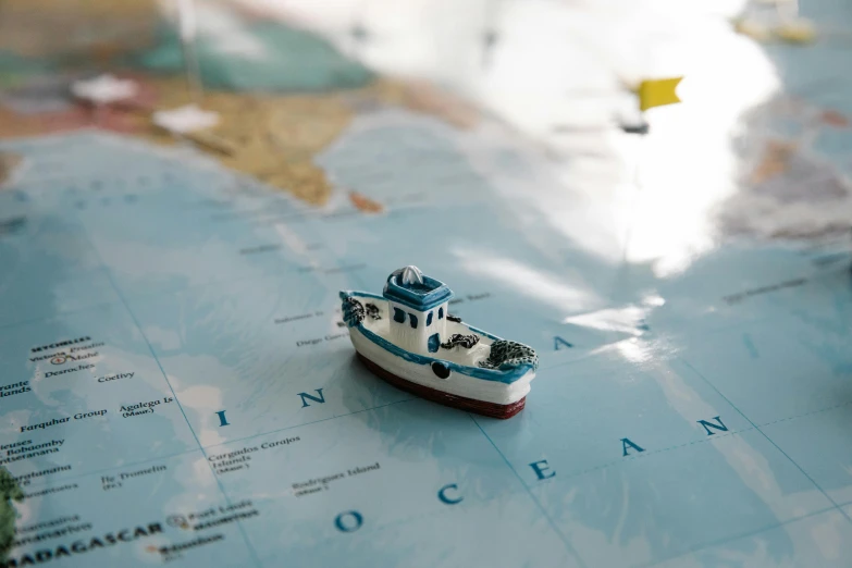 a toy boat sitting on top of a map, by Nick Fudge, unsplash, fishing boat, micro detail, coast, made of glazed