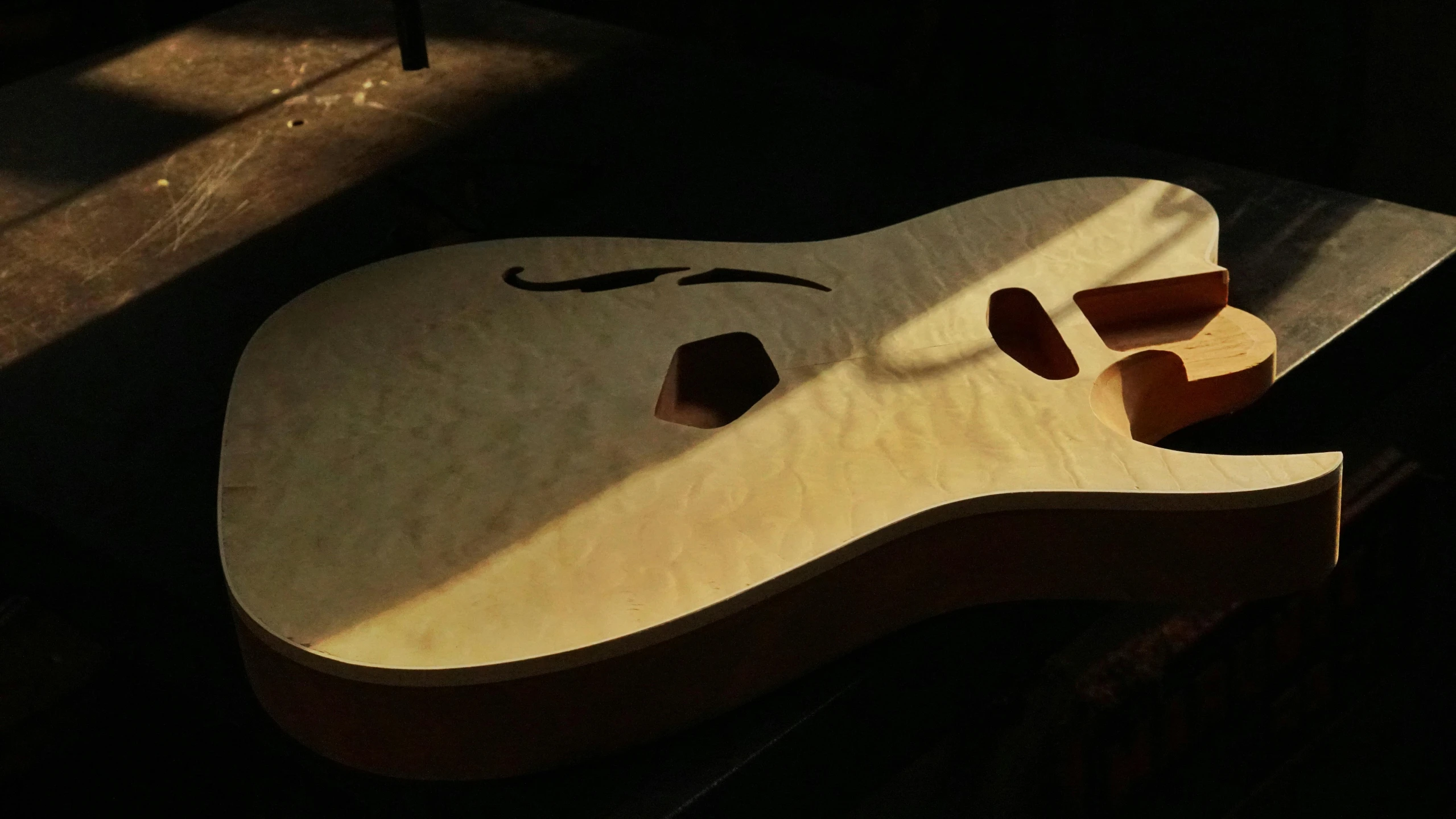 a guitar sitting on top of a wooden table, back lit, prototype, polished maple, volumetric lighting from above