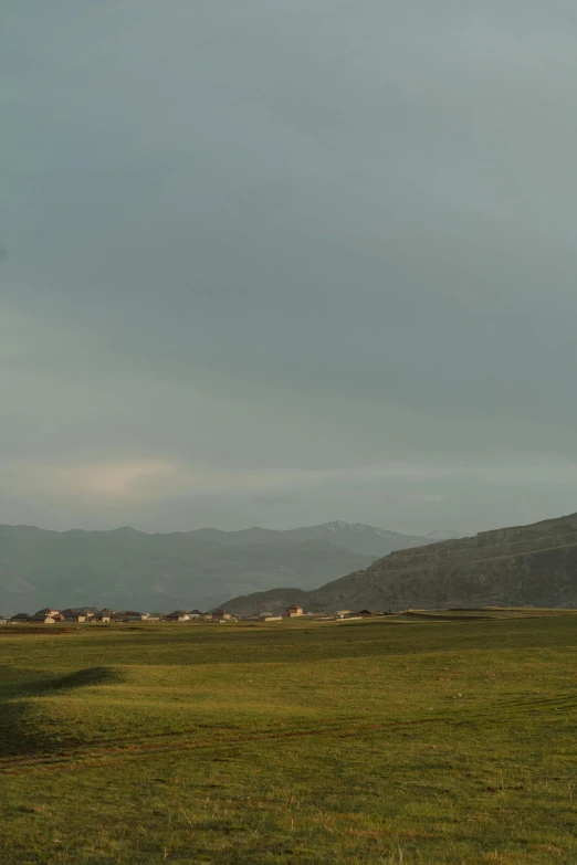 a man flying a kite on top of a lush green field, by Muggur, land art, remote icelandic village, it's getting dark, golf course, several cottages