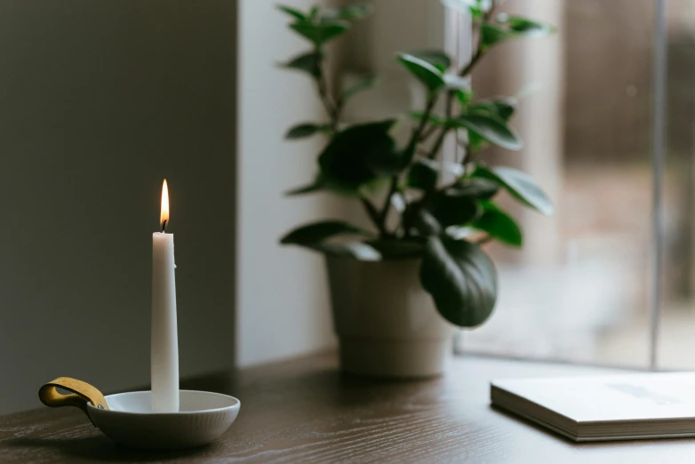 a white candle sitting on top of a wooden table, a still life, unsplash, dwell, with a long white, holding a candle holder, brightly-lit