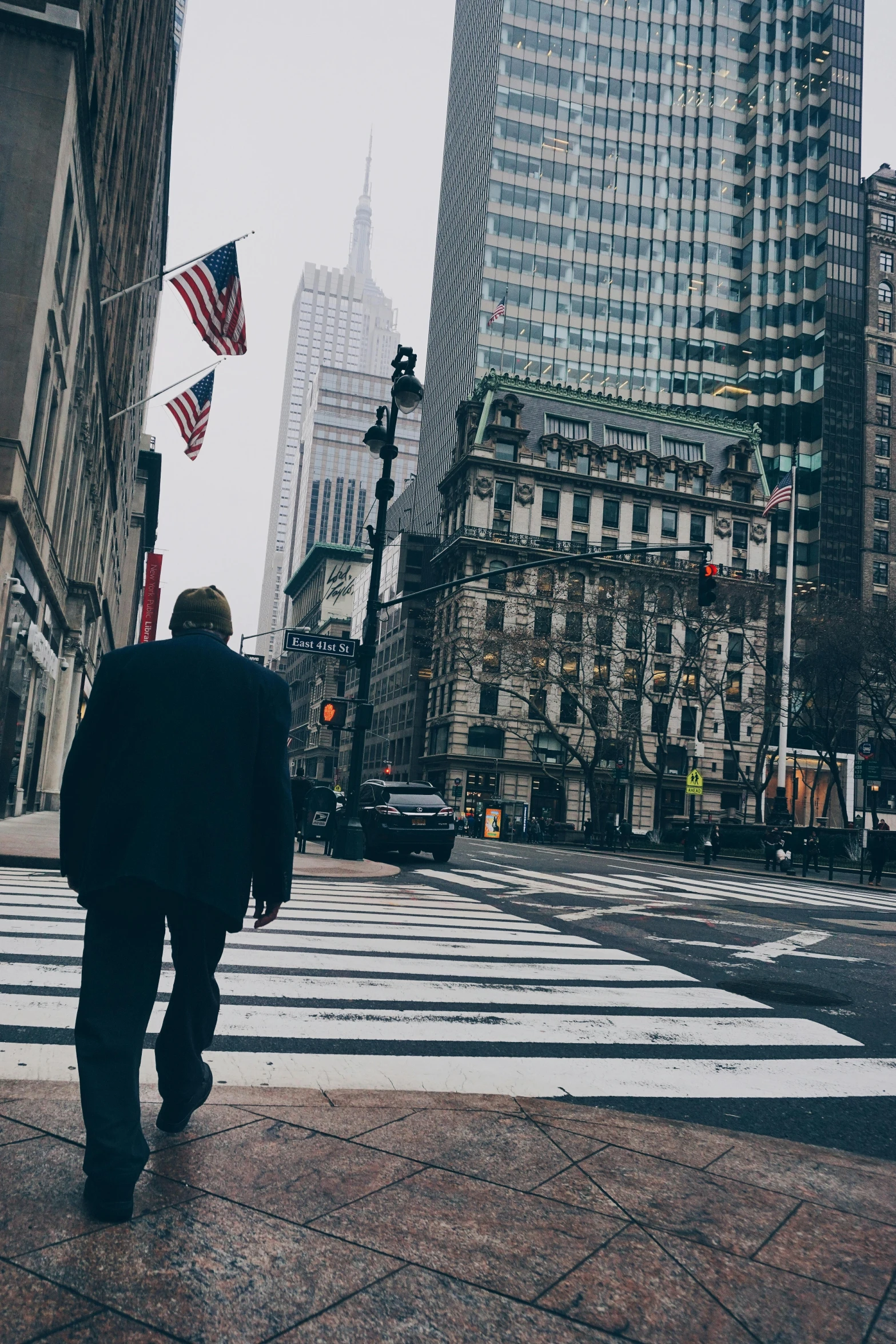 a man walking across a street next to tall buildings, inspired by Garry Winogrand, pexels contest winner, photo of donald trump, new jersey, crosswalks, low quality photo