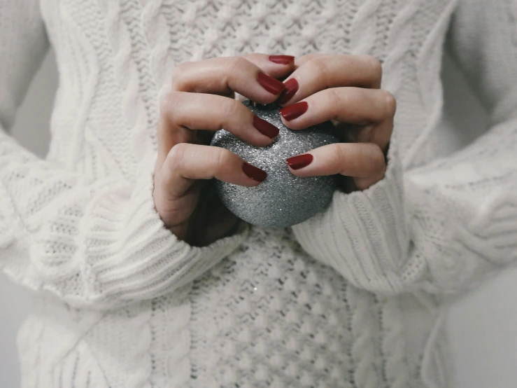 a woman in a white sweater holding a silver ornament, pexels contest winner, aestheticism, nail polish, silver red, holding a ball, holding each other hands