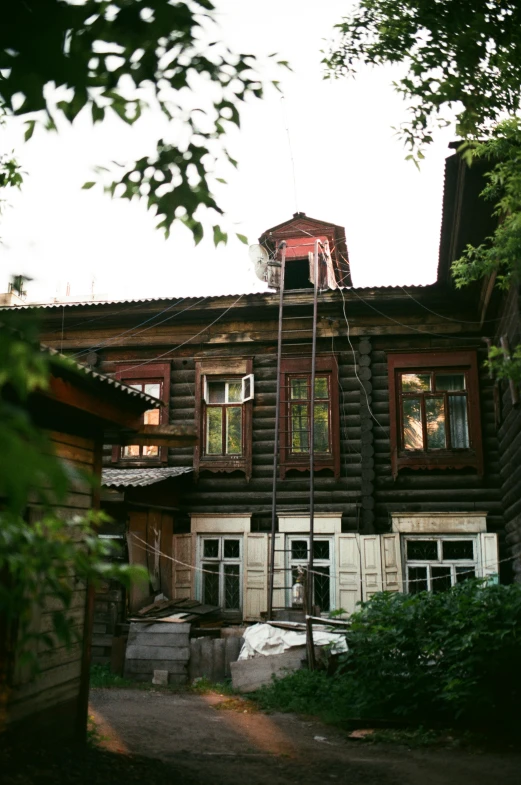 a man standing on a ladder in front of a house, an album cover, inspired by Mikhail Yuryevich Lermontov, surikov, 1990s photograph, cabin, lead - covered spire