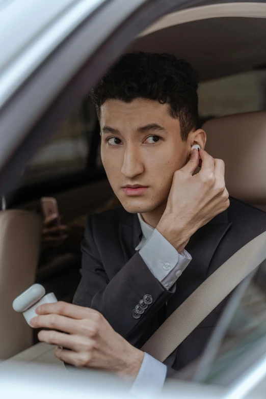 a man sitting in a car talking on a cell phone, an album cover, trending on pexels, photorealism, earbuds jewelry, asian man, wearing business suit, non binary model