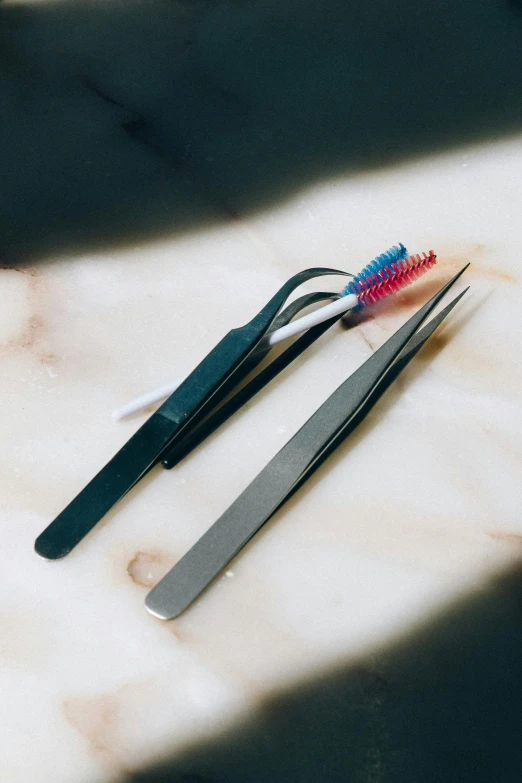 a pair of tweezers sitting on top of a marble counter, by Adam Marczyński, unsplash, various colors, curved blades on each hand, dentist, vessels