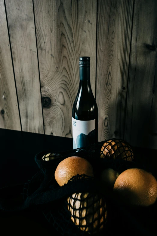 a bottle of wine and some oranges on a table, dark grey and orange colours, full body in shot, a fruit basket, full product shot