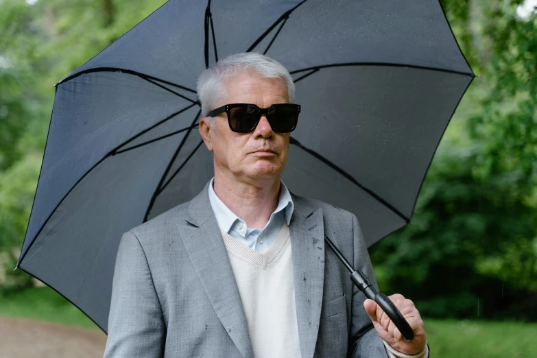 a man in a suit and sunglasses holding an umbrella, an album cover, unsplash, photorealism, gray haired, hammershøi, wolff olins, dramatic movie still