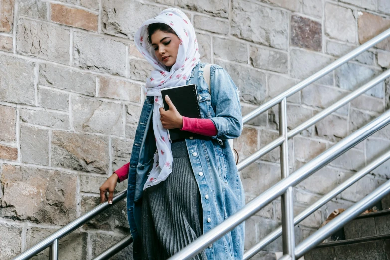 a woman in a hijab is walking up the stairs, trending on pexels, holding notebook, wearing double denim, wearing pink floral chiton, holding a giant book