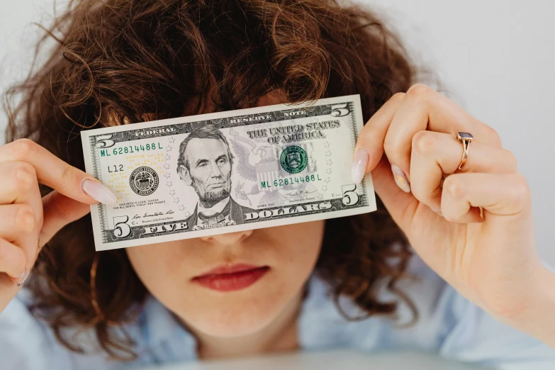 a woman covering her eyes with a dollar bill, a portrait, by Julia Pishtar, trending on unsplash, woman with braided brown hair, thumbnail, low fi, money sign pupils