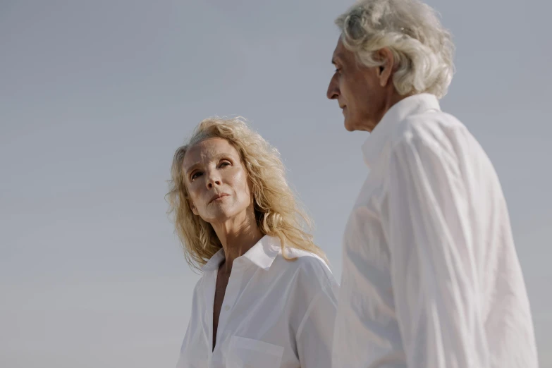 a man and a woman standing next to each other, unsplash, photorealism, curly white hair, 15081959 21121991 01012000 4k, white wrinkled shirt, looking into the distance