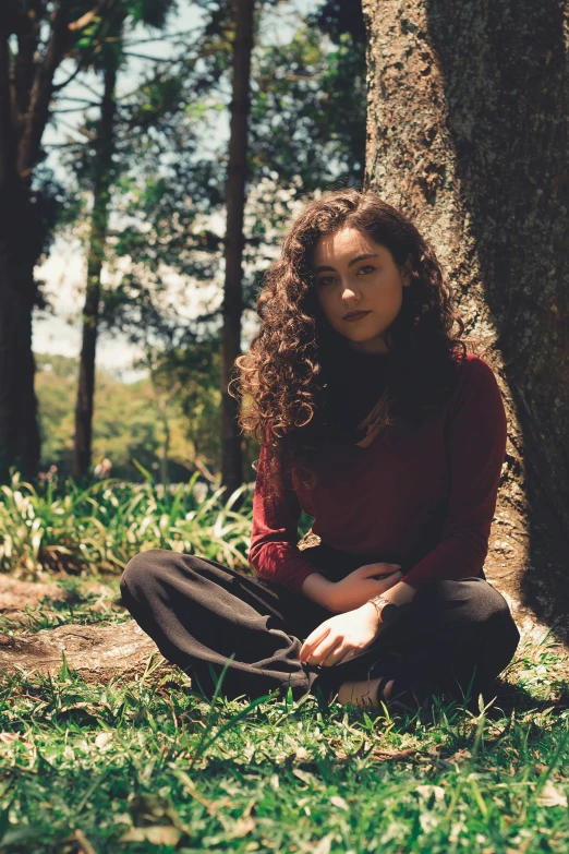 a woman sitting in the grass next to a tree, an album cover, inspired by Elsa Bleda, pexels contest winner, renaissance, brown curly hair, sydney park, casually dressed, instagram picture