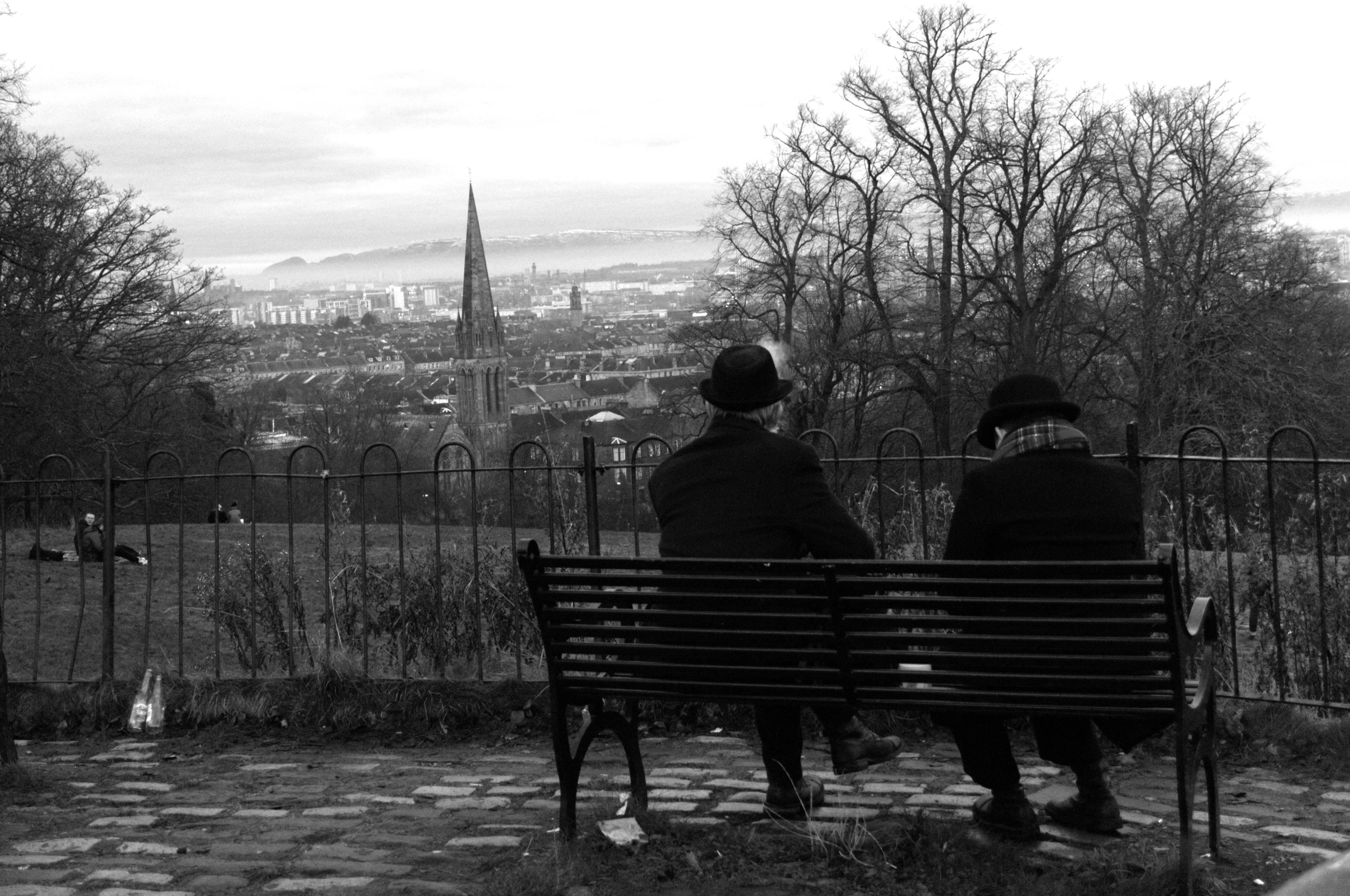 two people sitting on a bench overlooking a city, inspired by Bert Hardy, chesterfield, sad men, top of the hill, paisley