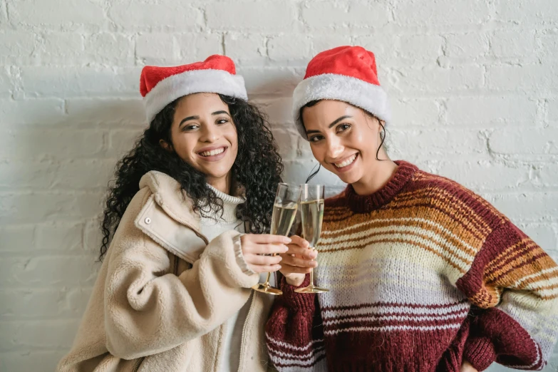 two women in santa hats holding glasses of champagne, pexels, diverse outfits, avatar image, background image, cosy vibes