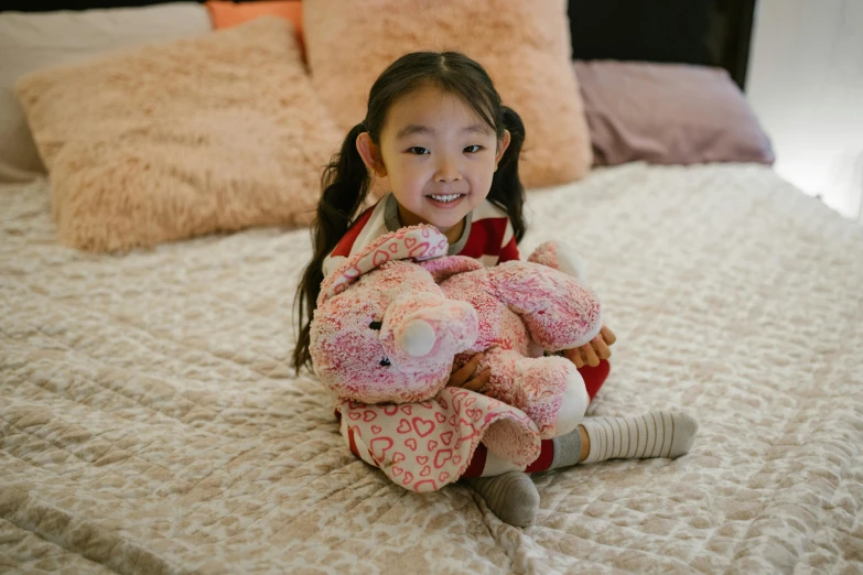 a little girl sitting on a bed holding a teddy bear, inspired by helen huang, wearing a pink rabbit costume, asian descent, stuffed dragon, smiling down from above