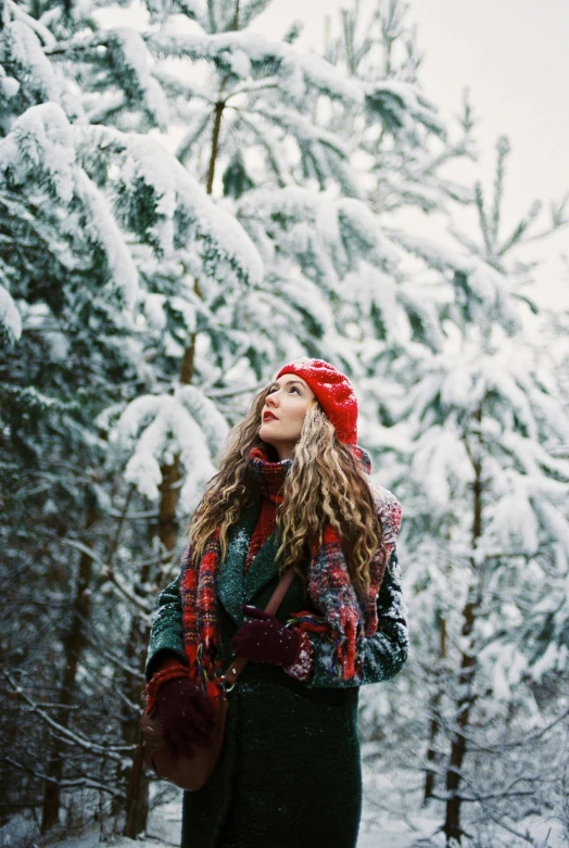 a woman standing in the middle of a snowy forest, red hat, looking to the sky, cool tousled hair, trending on