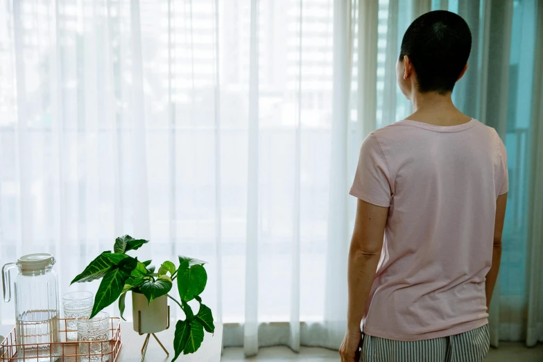 a woman standing in front of a window next to a potted plant, happening, set on singaporean aesthetic, back view. nuri iyem, curtains, anxiety environment