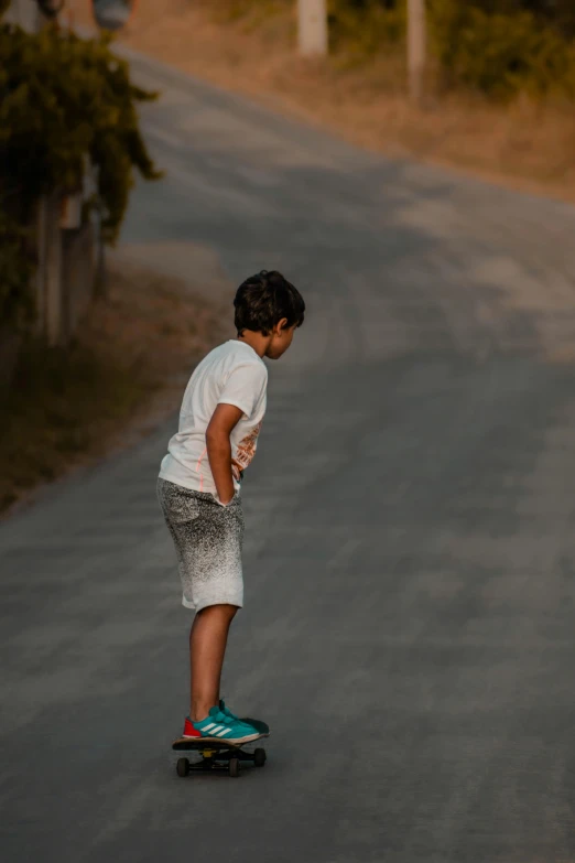 a young boy riding a skateboard down a road, by Max Dauthendey, pexels contest winner, happening, standing on a hill, soft texture, in a village, scratching head