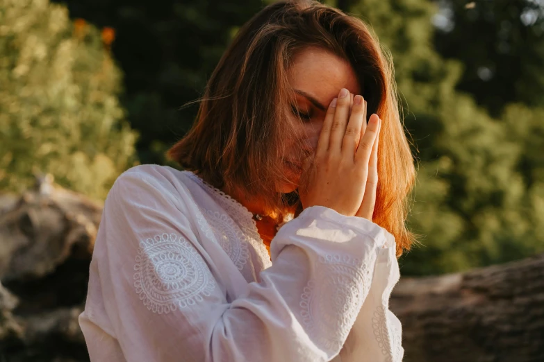 a woman covering her face with her hands, trending on pexels, wearing white robe, contemplative, wearing a blouse, magic hour