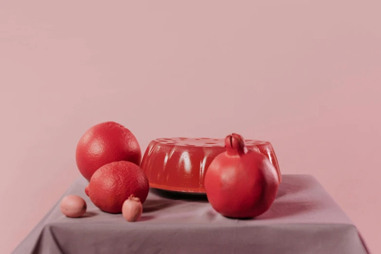 a red cake sitting on top of a table next to pomegranates, a still life, by Emma Andijewska, silicone skin, covered with pink marzipan, sleek round shapes, raytracing on