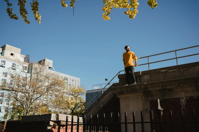 a man in a yellow shirt standing on a bridge, a photo, inspired by George Pirie, unsplash, parkour, standing on street corner, during autumn, city views