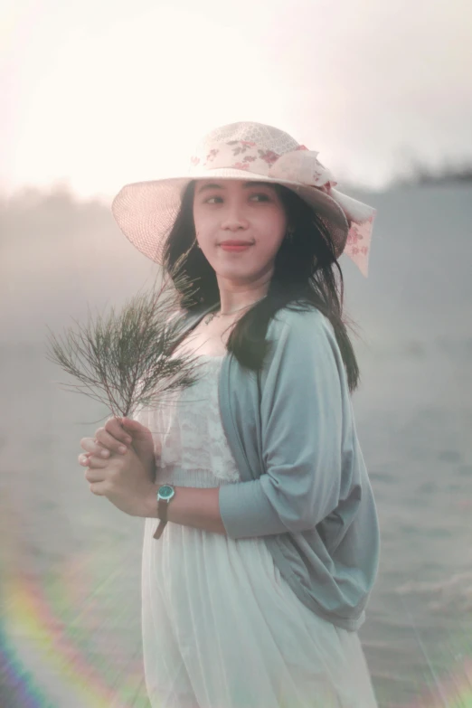 a woman standing on top of a beach holding a plant, a picture, inspired by Kim Du-ryang, unsplash, romanticism, wearing a light grey crown, portrait shot 8 k, soft evening lighting, pastel