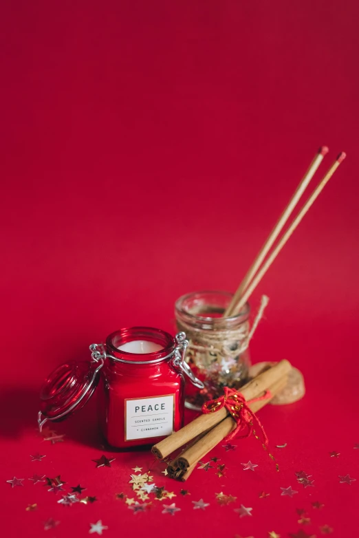 a candle and some cinnamon sticks on a red background, a picture, pexels, japanese collection product, peace, mid shot portrait, full product shot