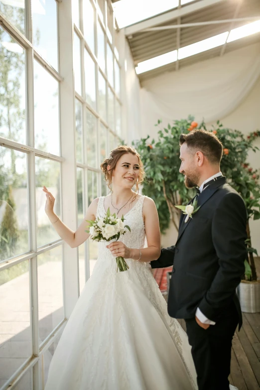 a man in a tuxedo standing next to a woman in a wedding dress, a picture, pexels contest winner, in bloom greenhouse, looking out open window, smiling slightly, ekaterina