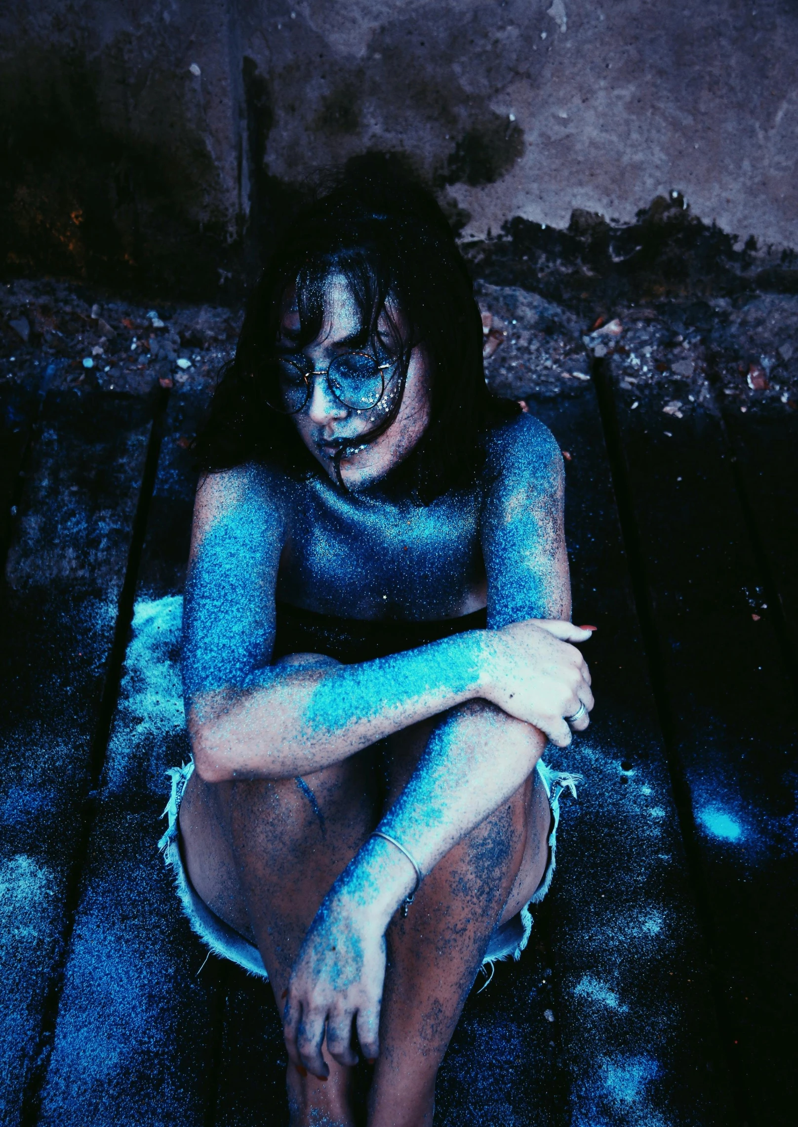 a woman sitting on the ground covered in blue paint, a colorized photo, inspired by Elsa Bleda, pexels contest winner, holography, with haunted eyes and dark hair, “uwu the prismatic person, instagram post, body horror