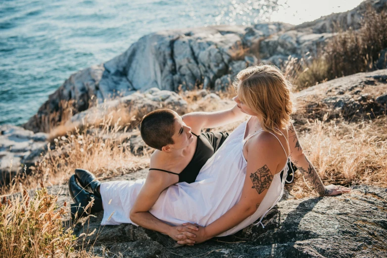 a man and woman sitting on a rock next to the ocean, pexels contest winner, happening, lesbian embrace, avatar image, casey cooke, flattened