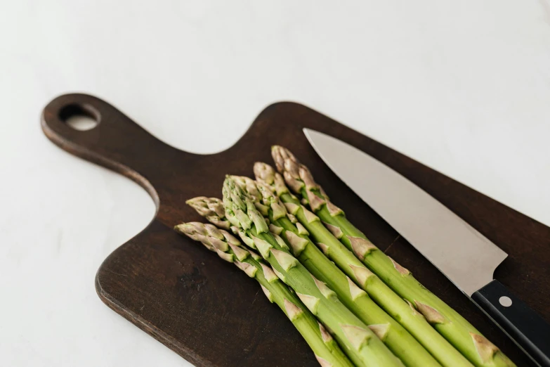 a bunch of asparagus on a cutting board with a knife, unsplash, detailed product image, upscaled to high resolution, portrait photo, paper