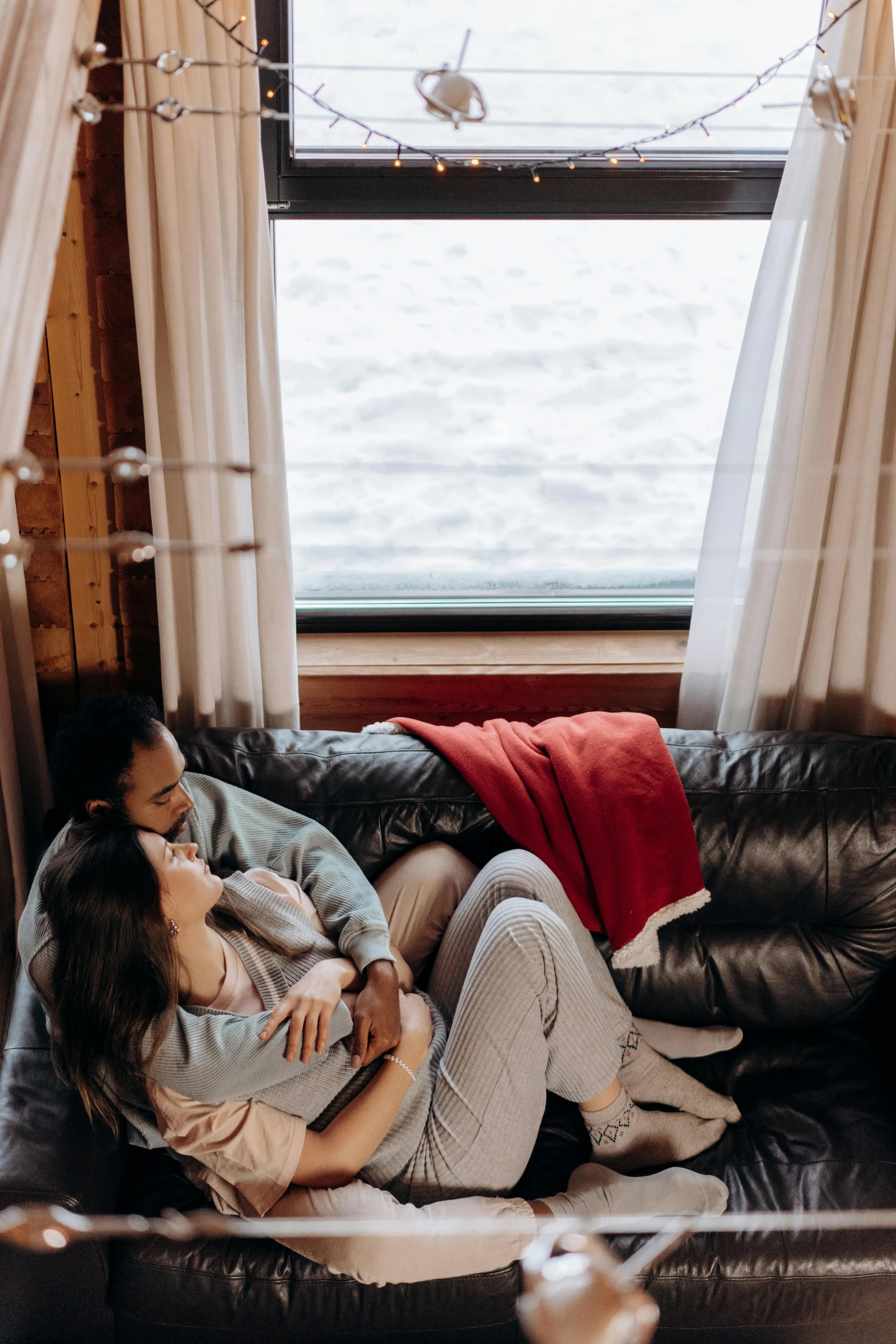 a man and woman sitting on a couch in front of a window, by Jan Tengnagel, pexels contest winner, ship interior, lake house, cuddling, holiday vibe