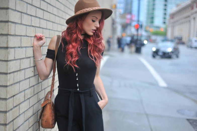 a woman with red hair leaning against a brick wall, inspired by Julia Pishtar, trending on pexels, black stetson hat, on a sidewalk of vancouver, jumpsuit, high details on clothes